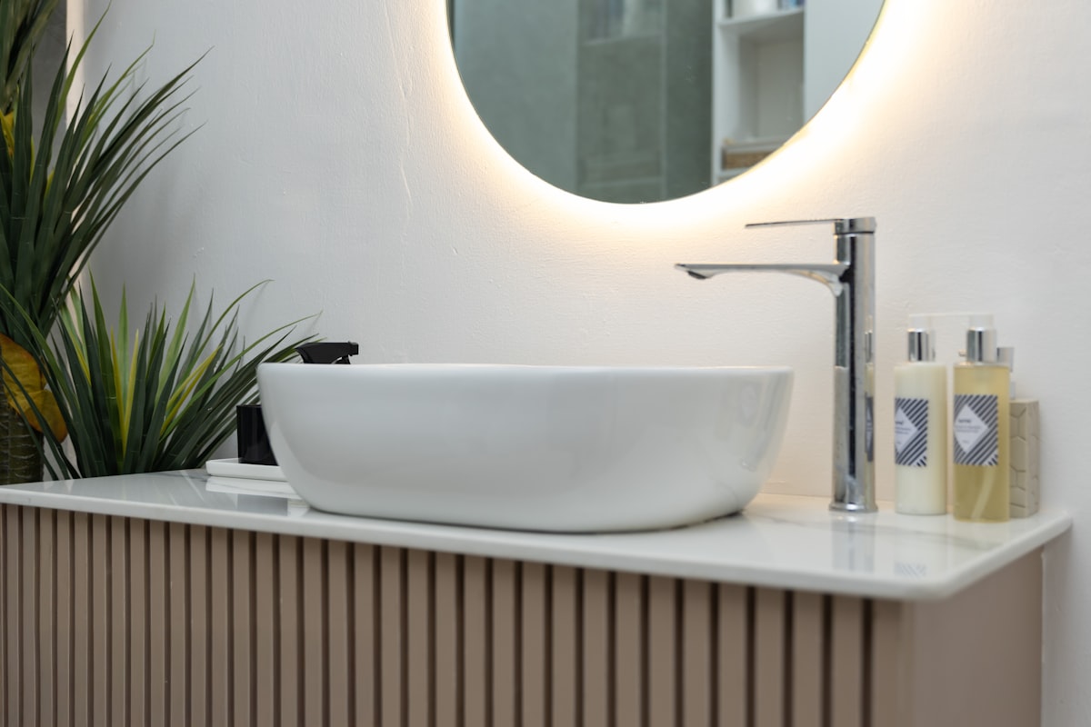 A white above-counter basin with a tall chrome mixer on a fluted vanity