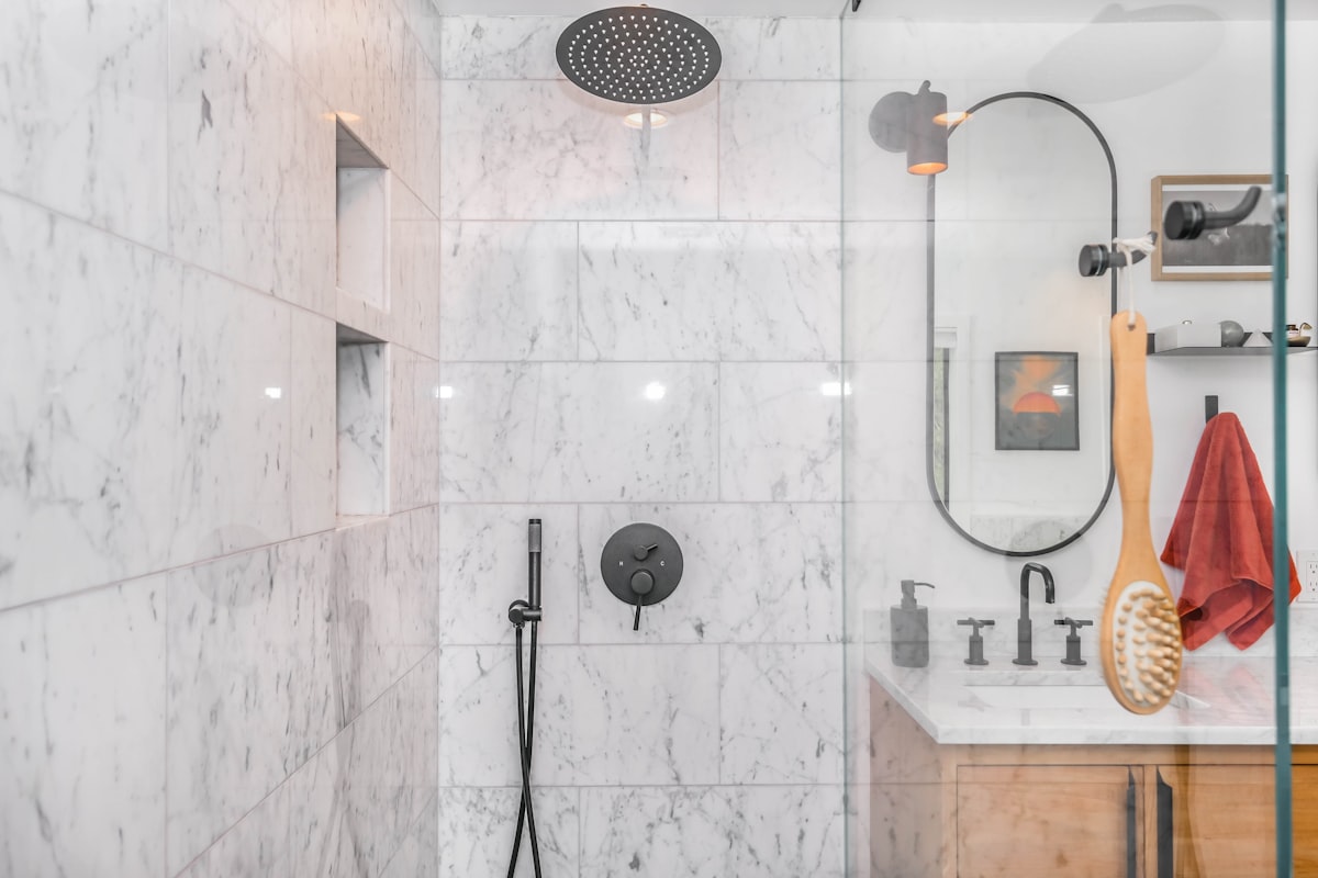 A matte black rain shower head, wall mixer and hand shower on marble tiling